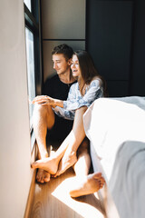 A man and a girl are sitting on the floor and are looking out the window