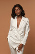 © Dmitry Tsvetkov - African american girl in white suit with wavy black hair and make-up posing on a beige background. Fashion style body length studio portrait. Elegant fashionable woman