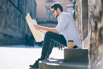 Wall Mural - Positive hipster guy in casual wear resting on old stairs during sightseeing tour in city