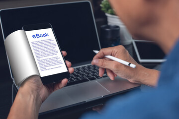 Casual man reading ebook via E reader app on mobile smart phone working on laptop computer at home