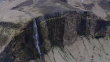 Orbiting Around The Front Of A Huge Cliff With A Tall Waterfall Trickling Down The Side Of A Mountain