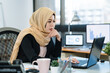 © PR Image Factory - Thoughtful worried muslim businesswoman in black suit and hijab with hand on chin looking at laptop computer screen in modern office. young islam lady worker frowning face confused thinking solution.