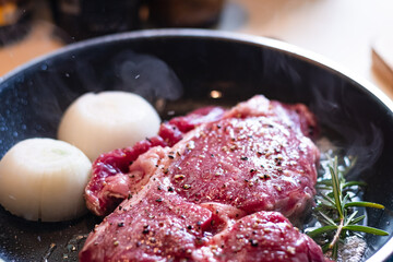 Poster - Cooking Juicy raw fresh red meat beef steak with chili pepper on top and onion in frying pan with smoke at the kitchen .