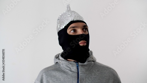 Portrait of a white frightened man in a black balaclava and a tinfoil hat  is afraid 5G waves. Thief or criminal in protective foil helmet. 5G tower radiation protection. Riots and marauding.