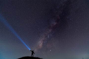 Silhouette of a man with a flashlight, observing beautiful, wide blue night sky with stars and Milky way galaxy. Astronomy, orientation, clear sky concept and background.