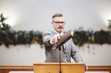 Poster - Male speaking near a wooden speech stand and holding a book in his hands