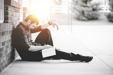 Wall Mural - Young male sitting on the ground and holding the bible in his hands