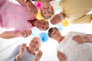 Wall Mural - Low angle of happy senior friends in the circle with balloons during birthday party