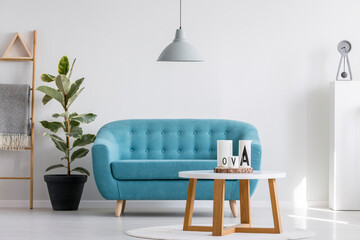 Wall Mural - Grey lamp above white wooden coffee table next to blue elegant couch in bright living room interior with plant in black pot and scandinavian ladder