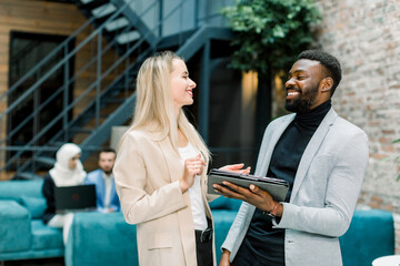 Wall Mural - Group of happy smiling multiethnical business people, pretty blond Caucasian woman and handsome bearded African man, standing together, laughing and enjoying work, sharing their ideas.