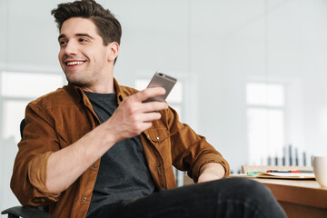 Poster - Image of joyful man smiling and using cellphone while drinking coffee