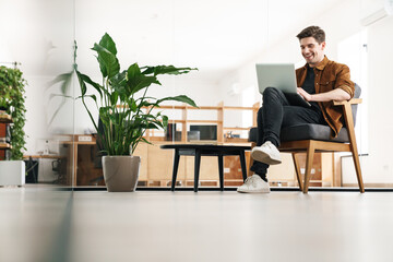 Wall Mural - Image of handsome happy caucasian man smiling while working with laptop