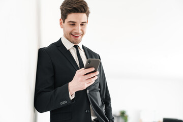 Wall Mural - Image of smiling businessman wearing black suit using mobile phone