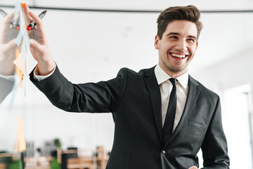 Poster - Image of concentrated young businessman wearing suit using stickers while working in office