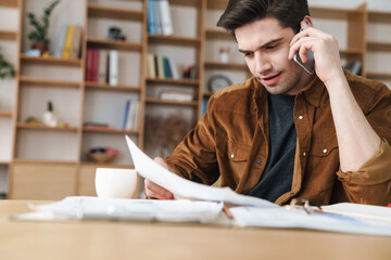 Wall Mural - Image of handsome man talking cellphone while working with documents