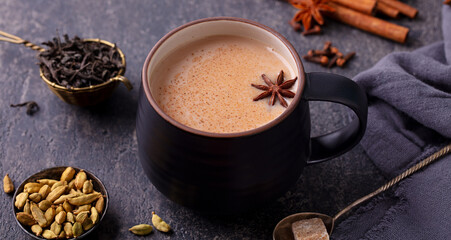 Wall Mural - Indian masala tea with milk and spices in mug. Grey background. Close up.