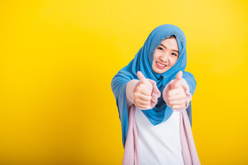 Wall Mural - Asian Muslim Arab, Portrait of happy beautiful young woman Islam religious wear veil hijab funny smile she made finger thumbs up, Ok sign to agree, studio shot isolated on yellow background