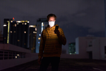 Poster - Young man with mask using phone against view of the city at night