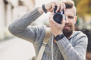 Young man photographer takes photographs with dslr camera in a city. Travel, vacations, professional freelance work and active lifestyle concept