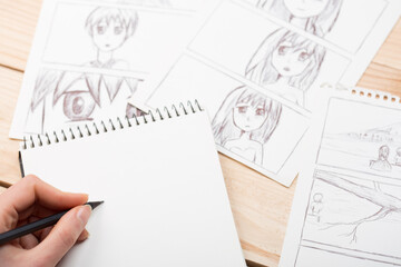 Wall Mural - Artist drawing an anime comic book in a studio. Wooden desk, natural light. Creativity and inspiration concept.