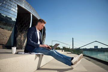 Young businessman sitting in the city outside in the sun we are working and holding a notebook, laptop