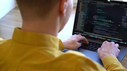 Wall Mural - young programmer businessman in a yellow shirt sitting at a wooden table and typing code on the keyb