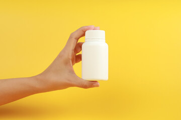 Wall Mural - Female hand holding a white plastic medicine bottle on yellow background