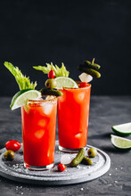 Bloody Mary Cocktail In Glasses With Garnishes. Tomato Bloody Mary Ice Cold Drink With Fresh Celery, Pickles And Lime