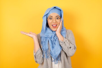 Canvas Print - Positive young beautiful muslim woman wearing hijab says: wow how exciting it is, has amazed expression, indicates something One hand on her head and pointing with other hand. Advertisement concept.