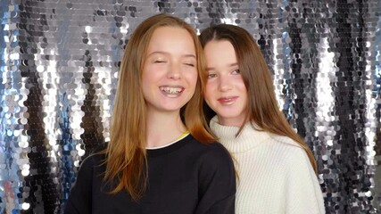 two girl teenager models with beautiful makeup laugh and pose for a photographer on a shiny silver b