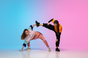 Wall Mural - Flexible. Sportive girls dancing hip-hop in stylish clothes on colorful gradient background at dance hall in neon light. Youth culture, movement, style and fashion, action. Fashionable portrait.