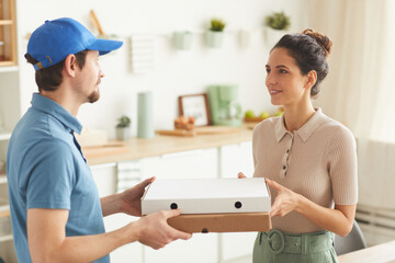 Wall Mural - Young man in uniform delivering pizza to young woman at home