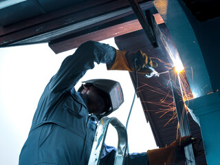 Industrial worker wearing safety mask, helmet, and safe glasses welding metal construction on factory. Industrial mechanic engineer working at the factory welding steel structure