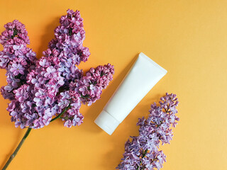 White plastic cosmetic bottle / tube for design labels and flowers lilac on an orange background. Unbranded lotion, balsam, hand creme. Top view.