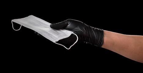 Wall Mural - Hand in black gloves holding disposable face mask isolated on black background