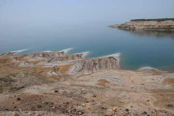 Dead Sea coast on the Jordanian side with salt deposits and bright blue water on a warm spring day, Dead Sea, Jordan