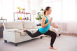 © Admiral - Young fitness woman doing lunges exercise is using furniture for workout at home. Sports training in living room. Copy space