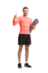 Fit man in sportswear holding an exercise mat and showing thumbs up