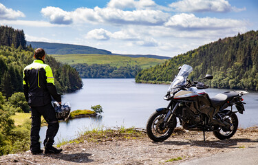 adventure motorcycle and biker man traveling, standing and watching landscape with lake and mountain