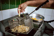 © stivog - Close-up of chef putting fries in deep fryer. Restaurant meal preparation