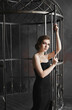Young beautiful woman in black dress gets out of the huge cage. Symbol of freedom and the ending of isolation.