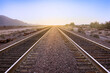 Two parallel rail road tracks vanishing on the horizon line and the golden setting sun