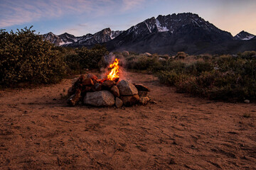 campfire in stone fire pit in desert at base of mountains with sunset sky