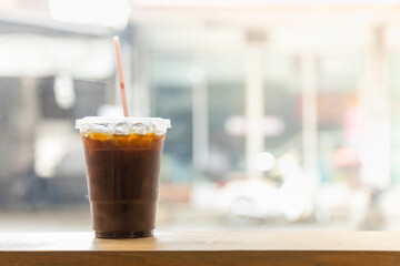 Wall Mural - Close up of take away plastic cup of iced black coffee (Americano) in restaurant on wooden table with copy sapce.