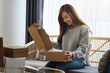 A beautiful young asian woman receiving and opening a postal parcel box at home for delivery and online shopping concept
