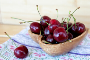 Wall Mural - Ripe red cherries in a wooden plate with a brown towel on a wooden background