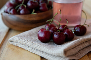 Wall Mural - Ripe red cherries in a wooden plate with a glass of juice  and a brown towel on a wooden background