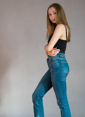 Wall Mural - Full body portrait of a pretty teenage girl wearing a black tank top and denim jeans standing looking at the camera. Studio shot