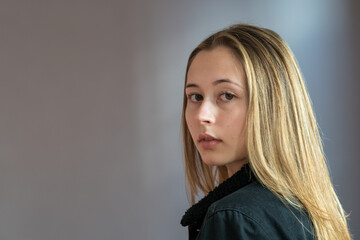 Wall Mural - Semi profile portrait of a pretty teenage girl with long natural blonde hair and smooth skin looking at the camera. Studio shot