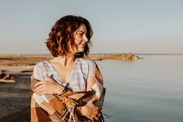 Concept of summer holidays at sea and live style. Young woman in blue dress  with a plaid  posing and walking  against the backdrop of a  sea. Photos on summer vacation